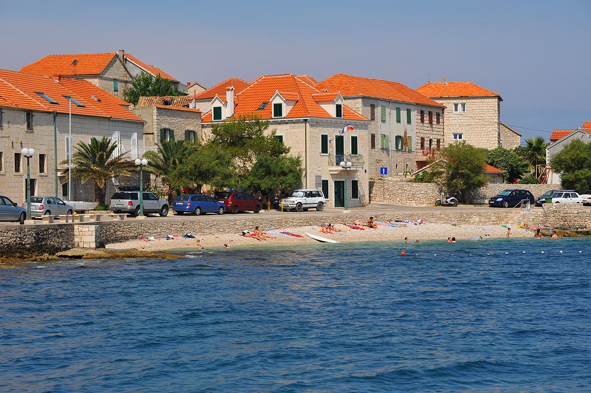 Blick vom Meer auf die Uferfront von Sutivan mit Steinhäusern, roten Dächern und Kieselstrand